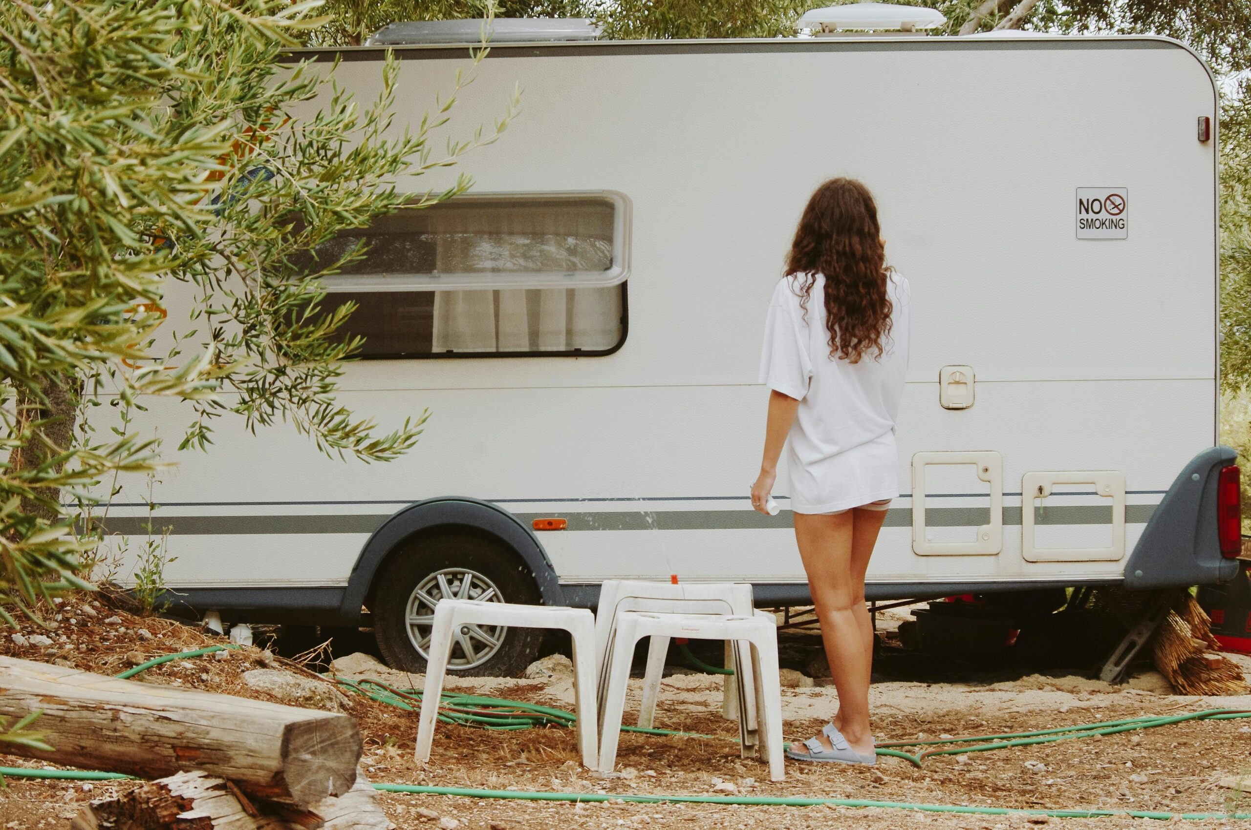A woman stands casually beside a camper trailer during summer outdoors.