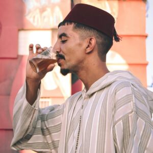 A Moroccan man in traditional attire enjoying mint tea against a colorful street art background.
