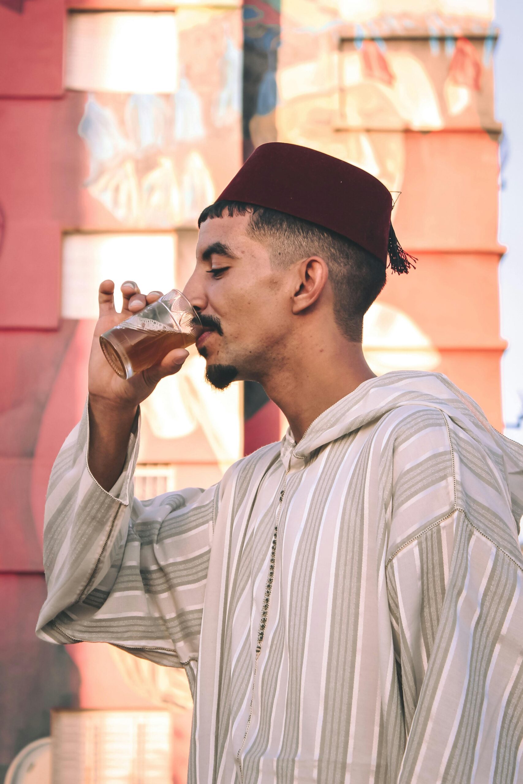 A Moroccan man in traditional attire enjoying mint tea against a colorful street art background.